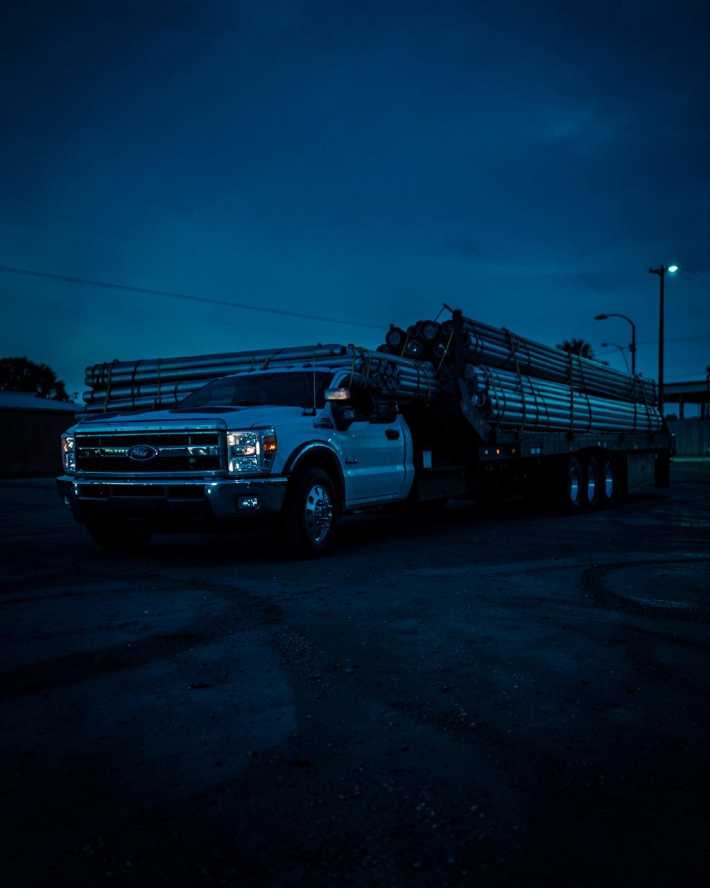 One-ton dually pickup pulling a loaded gooseneck flatbed trailer at dusk